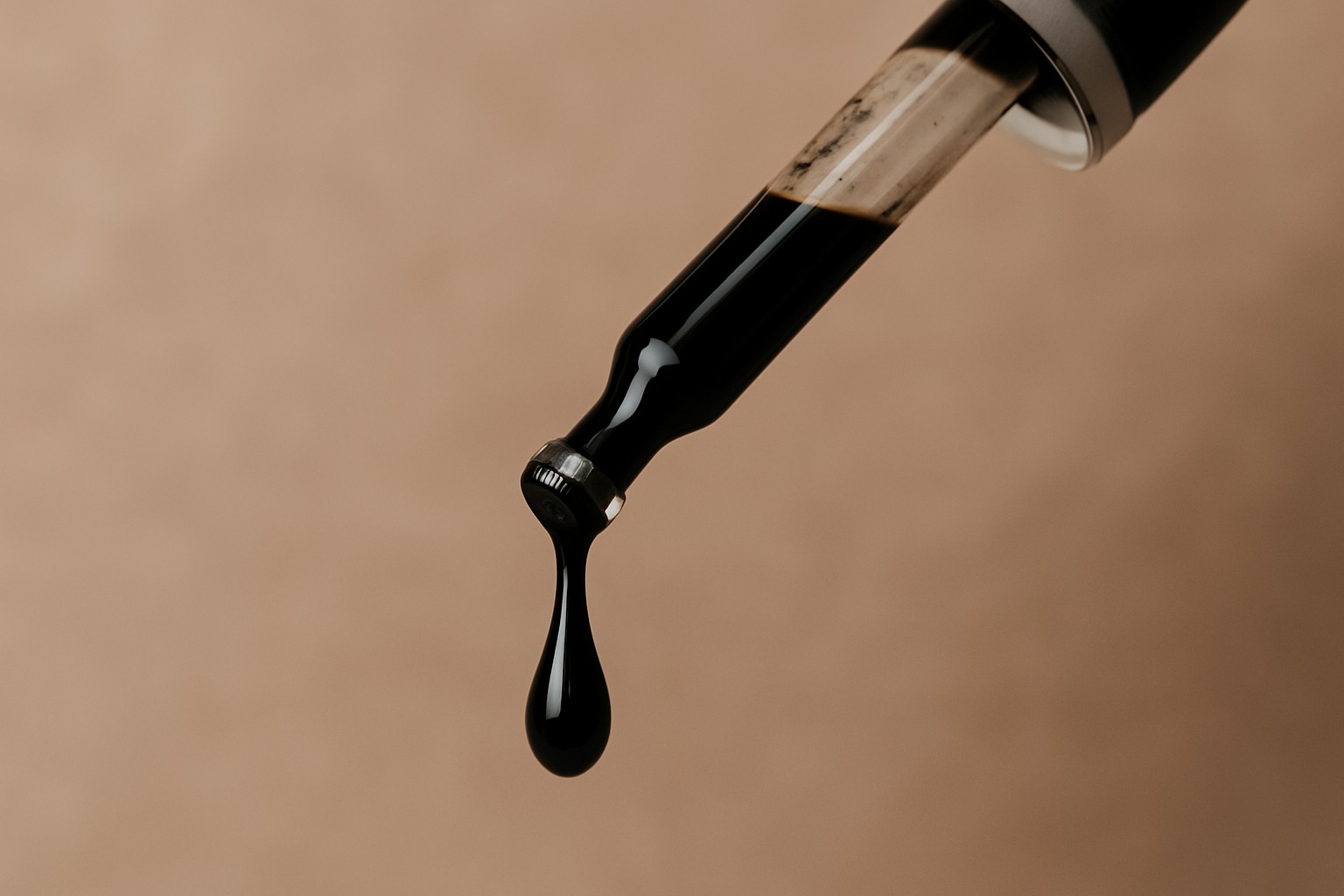 Close-up of liquid Shilajit dripping from a glass dropper into a small amber bottle
